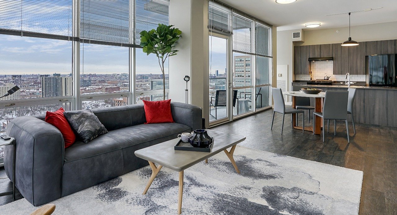 Bright living room and kitchen combo with expansive city views, modern decor, and comfortable seating at Arrive LEX in Chicago