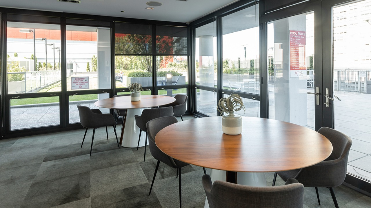 Bright community dining lounge with round tables, modern chairs, and large windows leading to an outdoor patio at Arrive LEX in Chicago