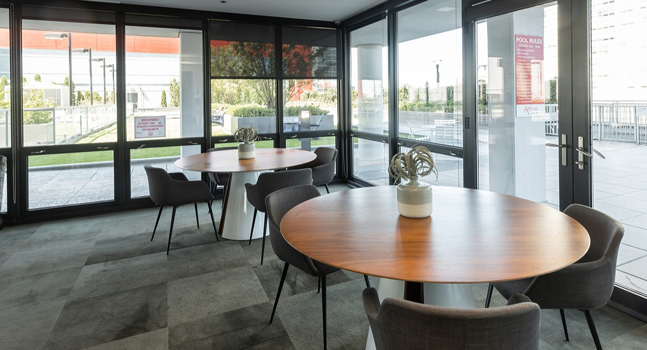 Bright community dining lounge with round tables, modern chairs, and large windows leading to an outdoor patio at Arrive LEX in Chicago