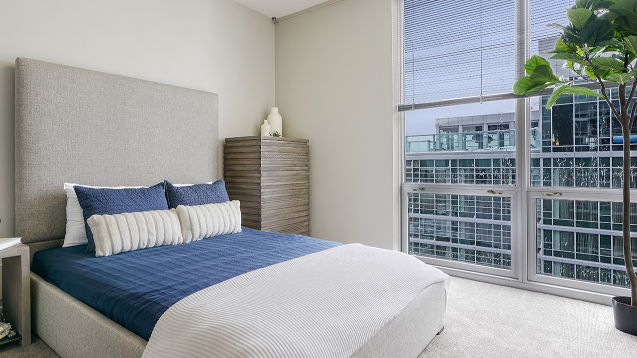 Cozy bedroom featuring a large window with city views, a comfortable bed with blue and white linens, and modern decor at Arrive LEX in Chicago