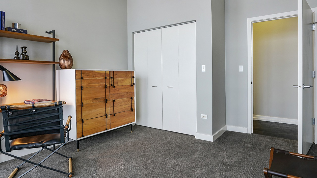 Flexible den or office space with shelving, a modern desk, a unique wooden dresser, and ample closet space at Arrive LEX in Chicago