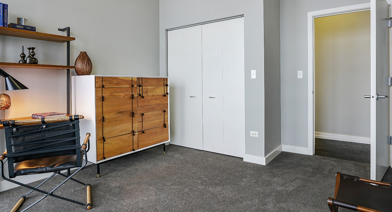 Flexible den or office space with shelving, a modern desk, a unique wooden dresser, and ample closet space at Arrive LEX in Chicago
