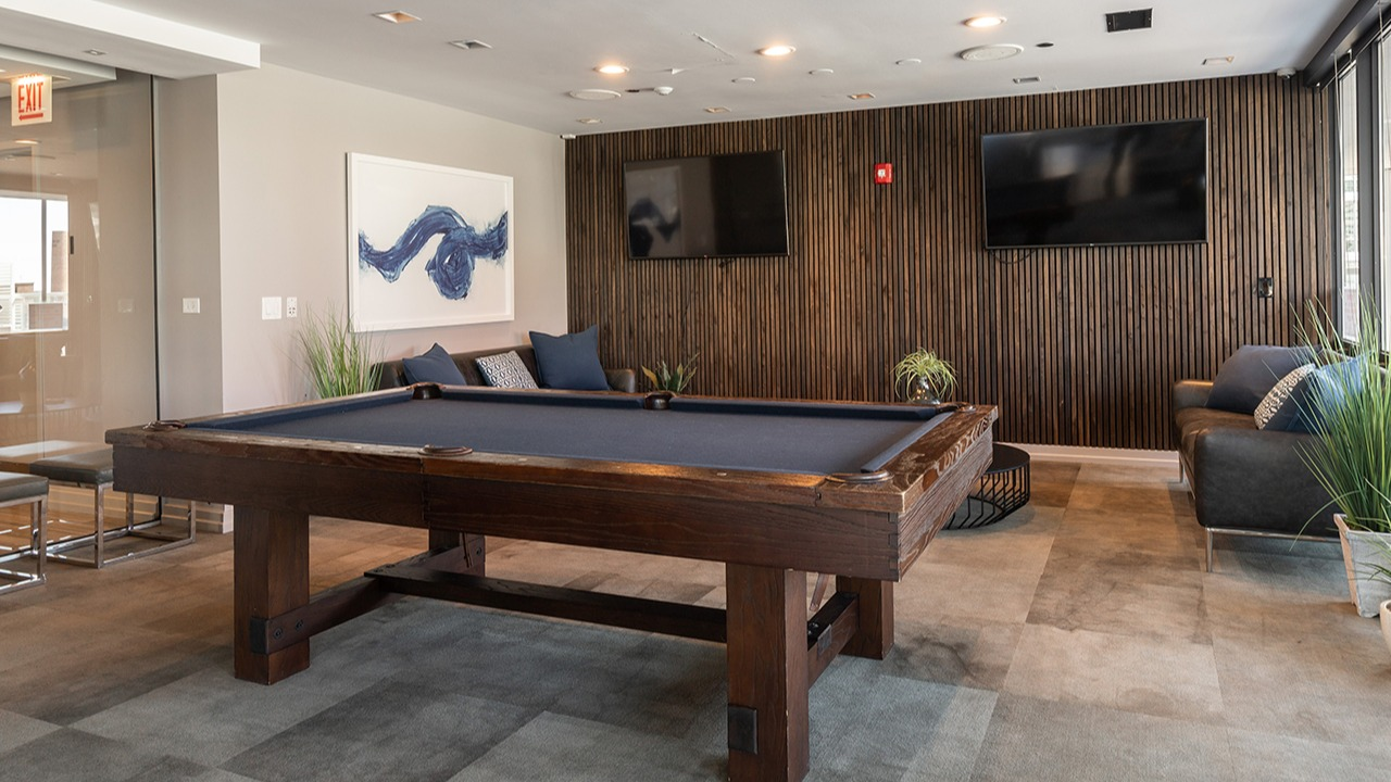 Stylish game room and lounge featuring a large pool table, comfortable seating, wall-mounted TVs, and modern decor at Arrive LEX in Chicago