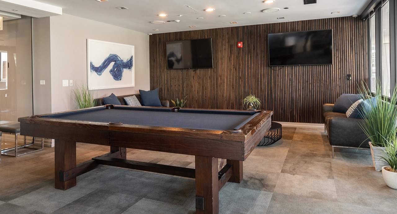 Stylish game room and lounge featuring a large pool table, comfortable seating, wall-mounted TVs, and modern decor at Arrive LEX in Chicago