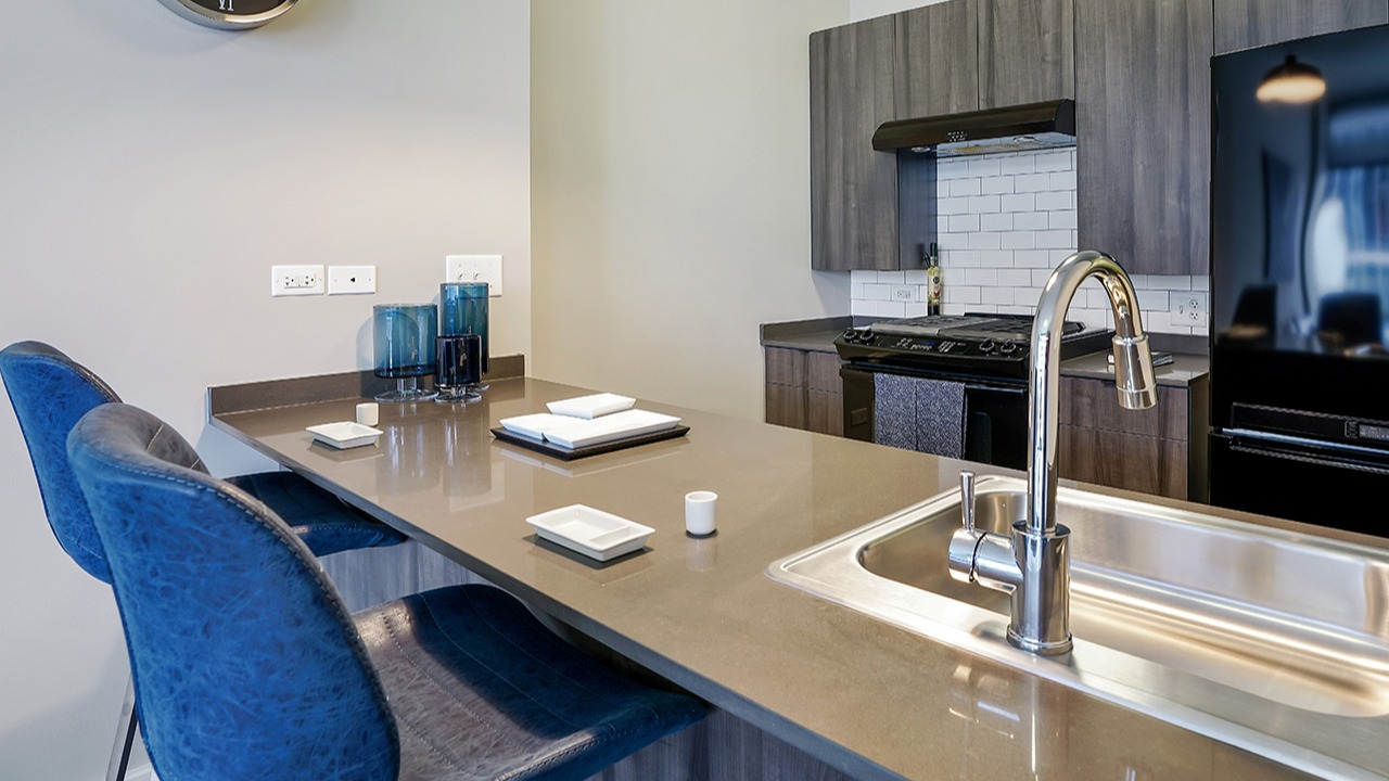 Gourmet kitchen with sleek black appliances, modern cabinetry, a spacious island with bar seating, and a stylish sink at Arrive LEX in Chicago