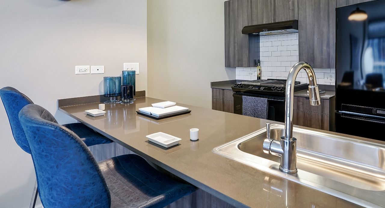 Gourmet kitchen with sleek black appliances, modern cabinetry, a spacious island with bar seating, and a stylish sink at Arrive LEX in Chicago