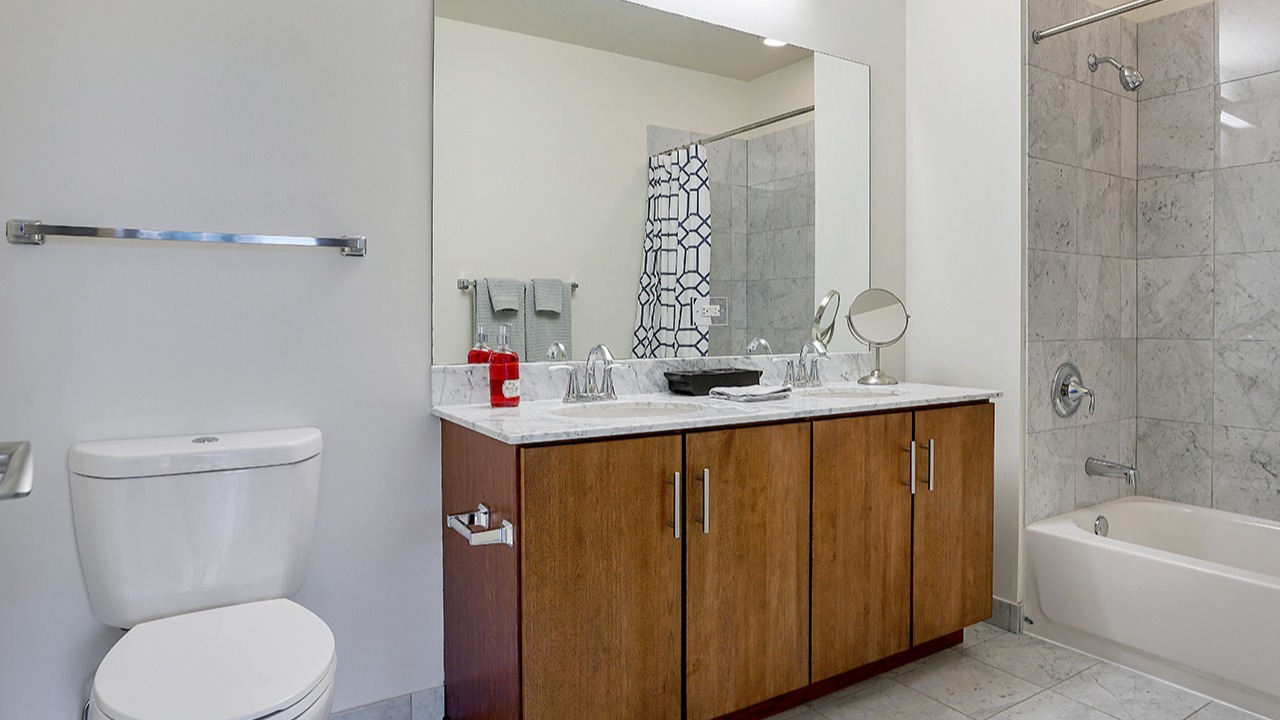 Modern bathroom with a large mirror, dual sinks, white shower tiles, and a patterned shower curtain at Arrive LEX in Chicago