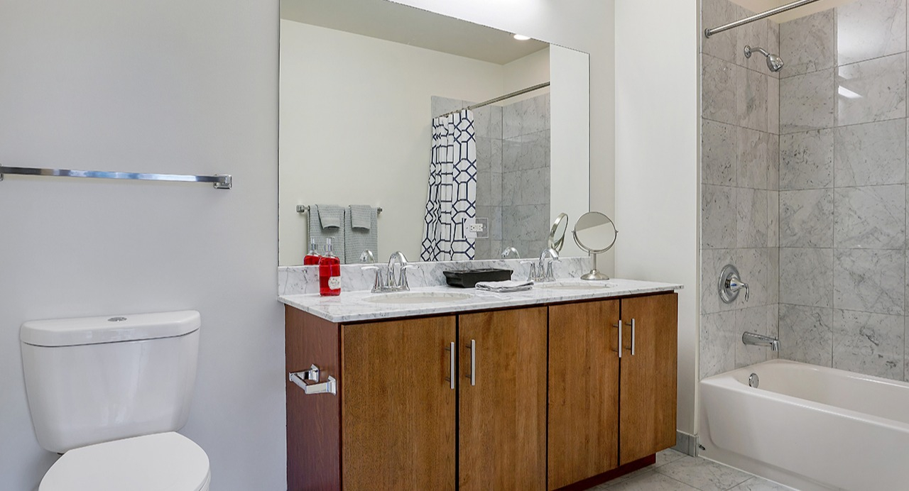 Modern bathroom with a large mirror, dual sinks, white shower tiles, and a patterned shower curtain at Arrive LEX in Chicago