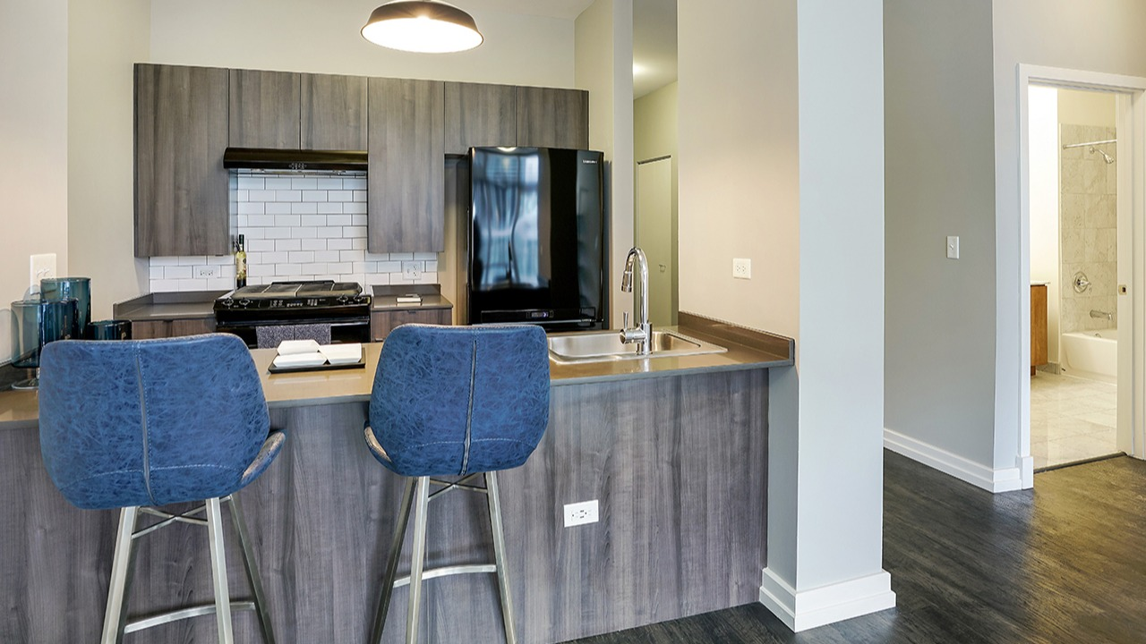 Modern kitchen with sleek appliances, wood cabinetry, and a breakfast bar, leading to a spacious hallway at Arrive LEX in Chicago