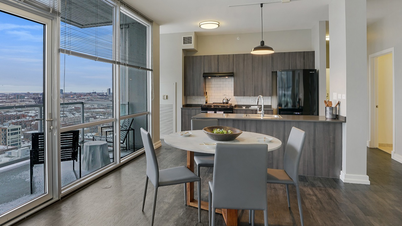 Open-concept kitchen and dining area with modern appliances, stylish cabinetry, a dining table, and large windows at Arrive LEX in Chicago