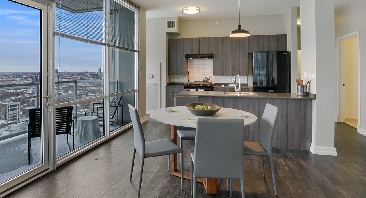 Open-concept kitchen and dining area with modern appliances, stylish cabinetry, a dining table, and large windows at Arrive LEX in Chicago