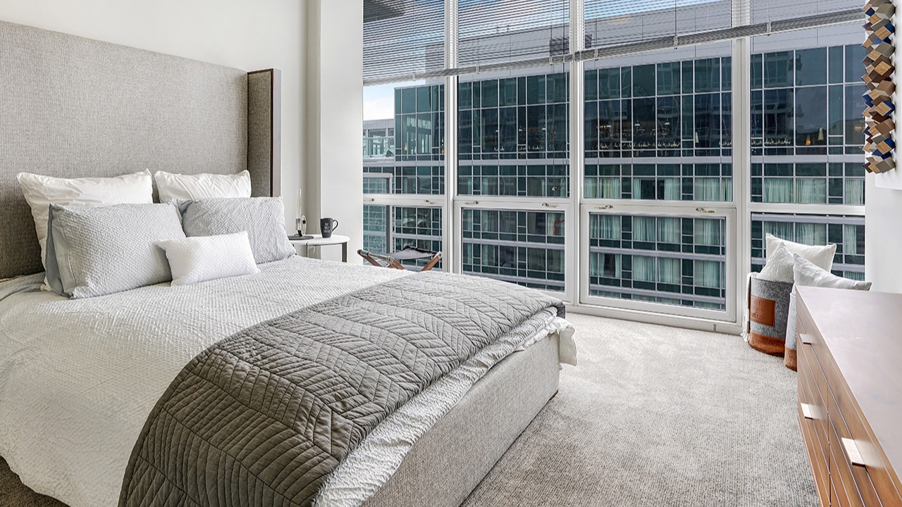 Spacious bedroom with a large window offering city views, a large bed with neutral bedding, and elegant furnishings at Arrive LEX in Chicago