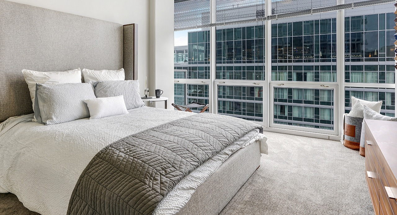 Spacious bedroom with a large window offering city views, a large bed with neutral bedding, and elegant furnishings at Arrive LEX in Chicago