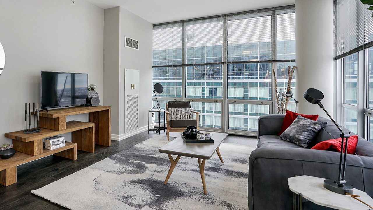 Stylish living room with a comfortable sofa, modern coffee table, entertainment center, and large windows offering city views at Arrive LEX in Chicago
