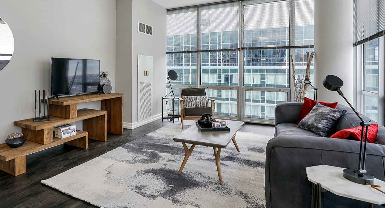 Stylish living room with a comfortable sofa, modern coffee table, entertainment center, and large windows offering city views at Arrive LEX in Chicago