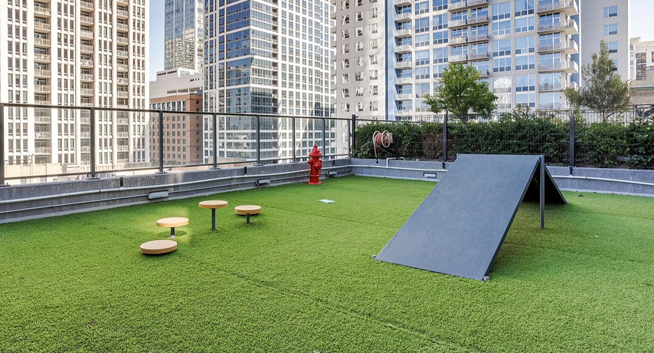 Outdoor dog run with artificial grass and agility equipment, offering city views at Arrive Michigan Avenue apartments in Chicago
