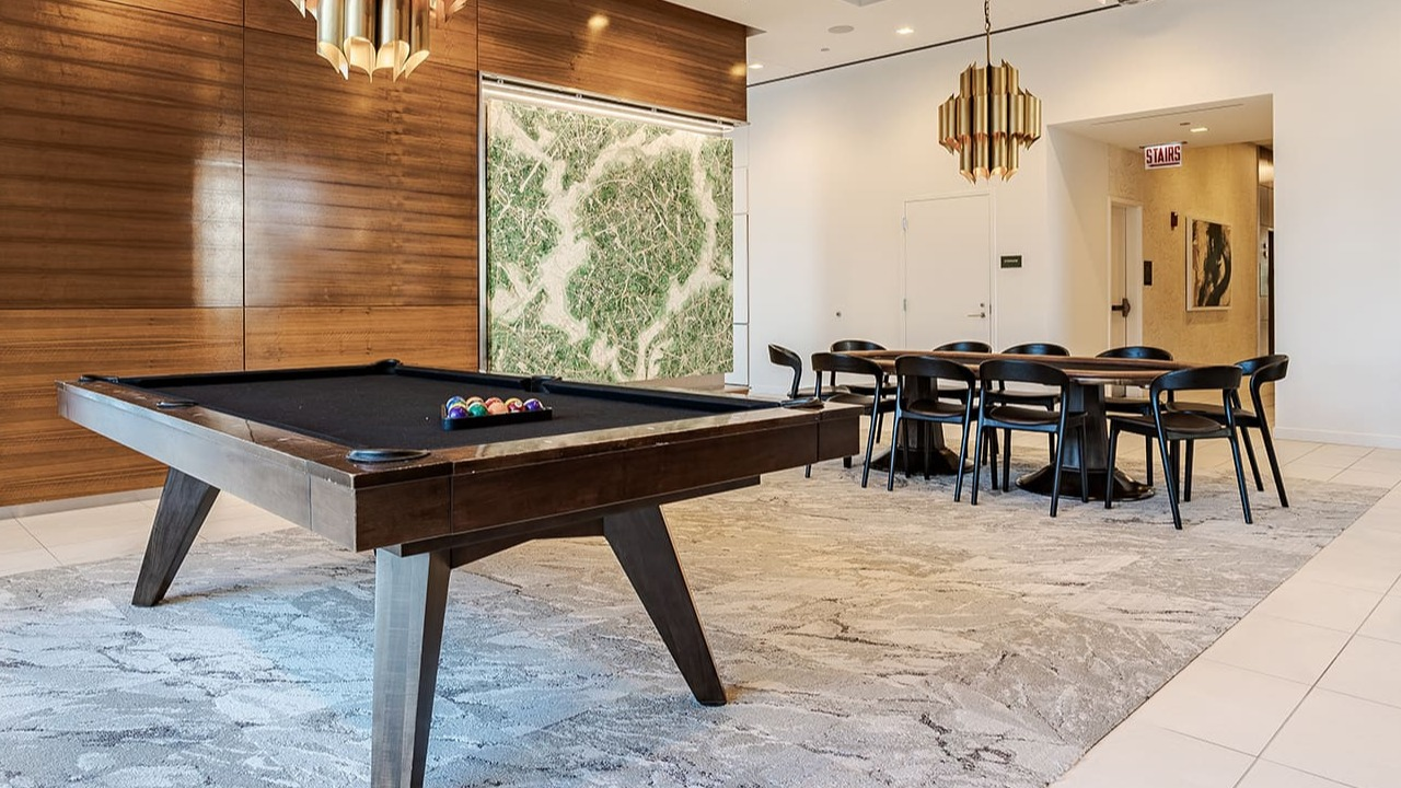 Stylish resident game room with a billiards table, modern chandeliers, and a dining area at Arrive Michigan Avenue in Chicago