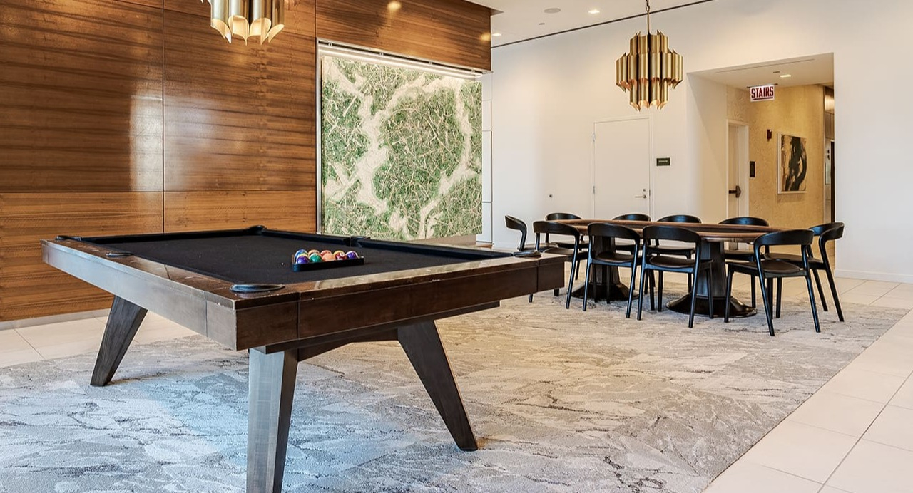 Stylish resident game room with a billiards table, modern chandeliers, and a dining area at Arrive Michigan Avenue in Chicago