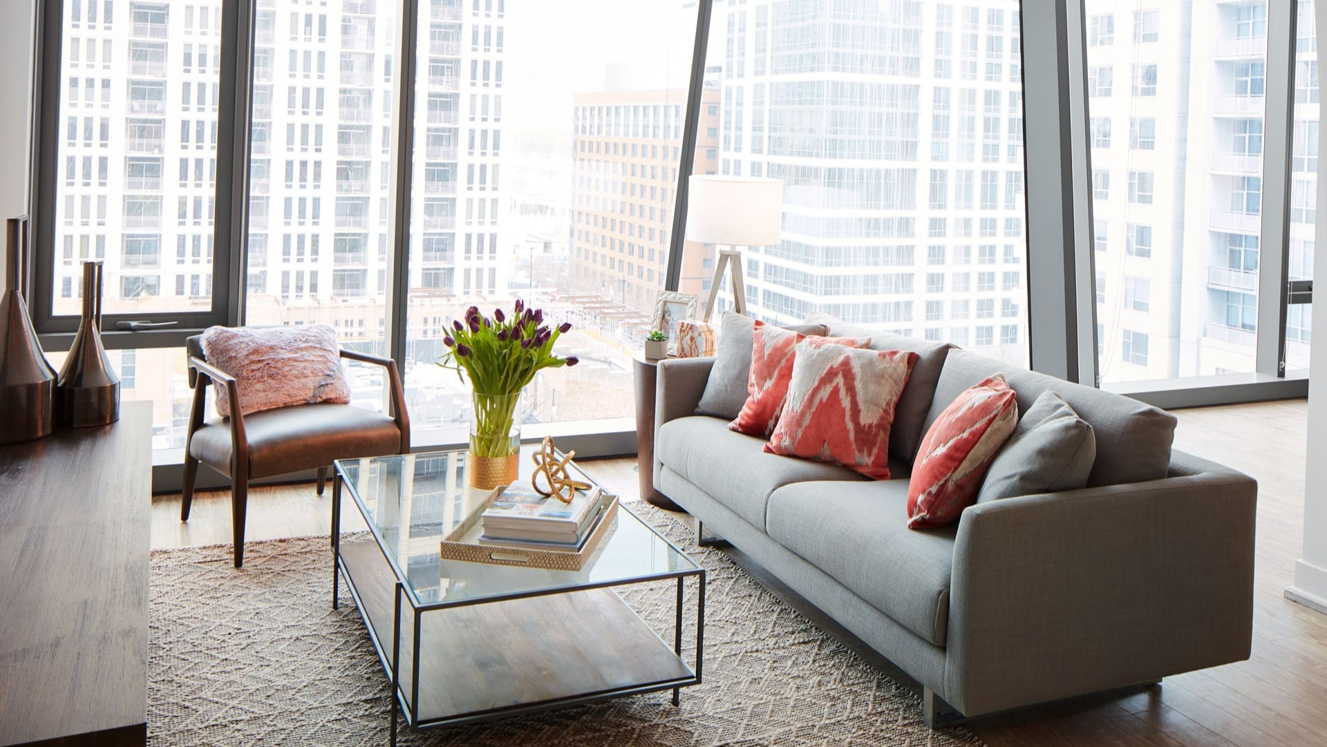 A bright and spacious living room with large windows, modern grey sofa, and stylish decor at Arrive Michigan Avenue apartments in Chicago