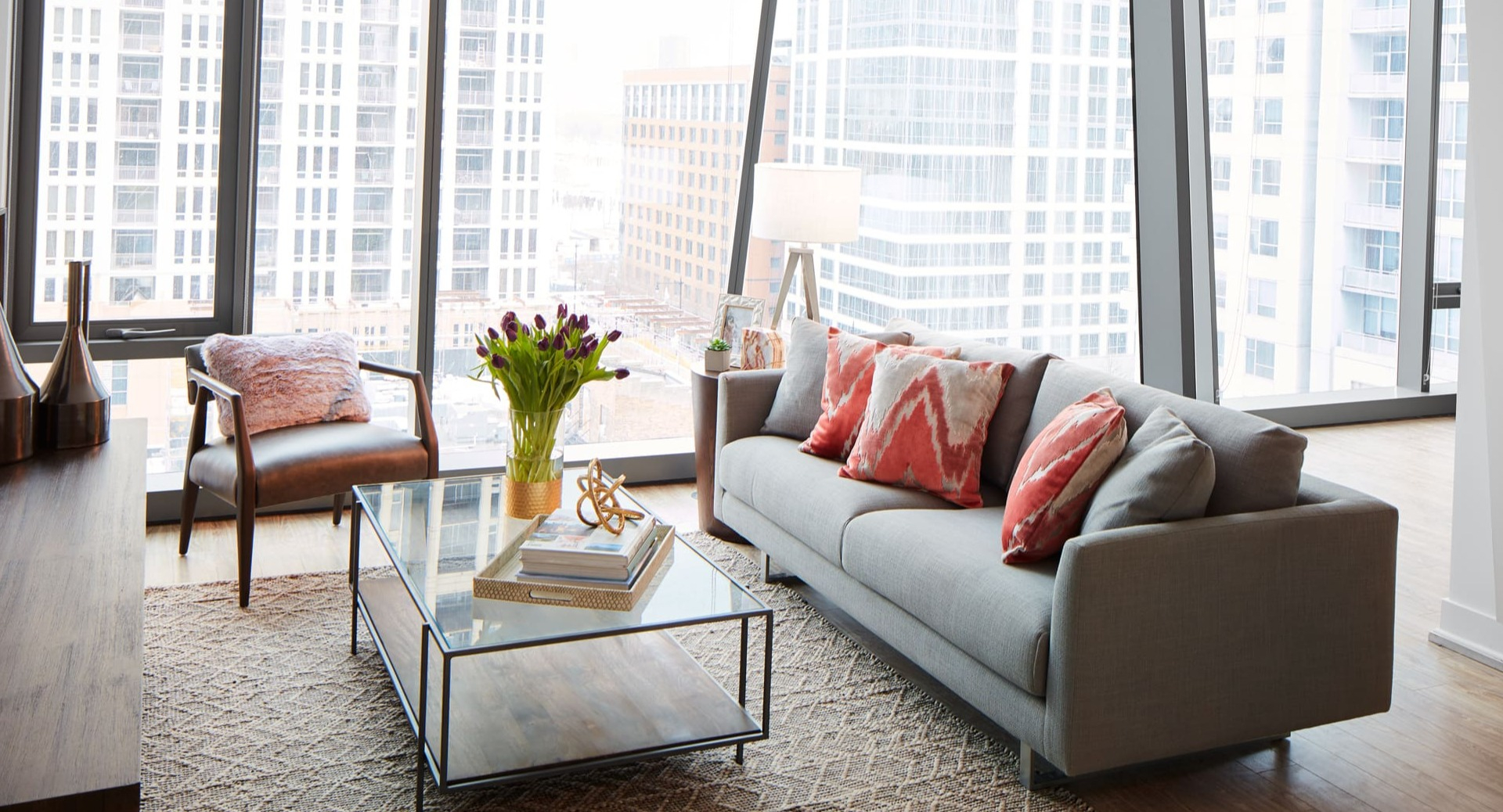 A bright and spacious living room with large windows, modern grey sofa, and stylish decor at Arrive Michigan Avenue apartments in Chicago