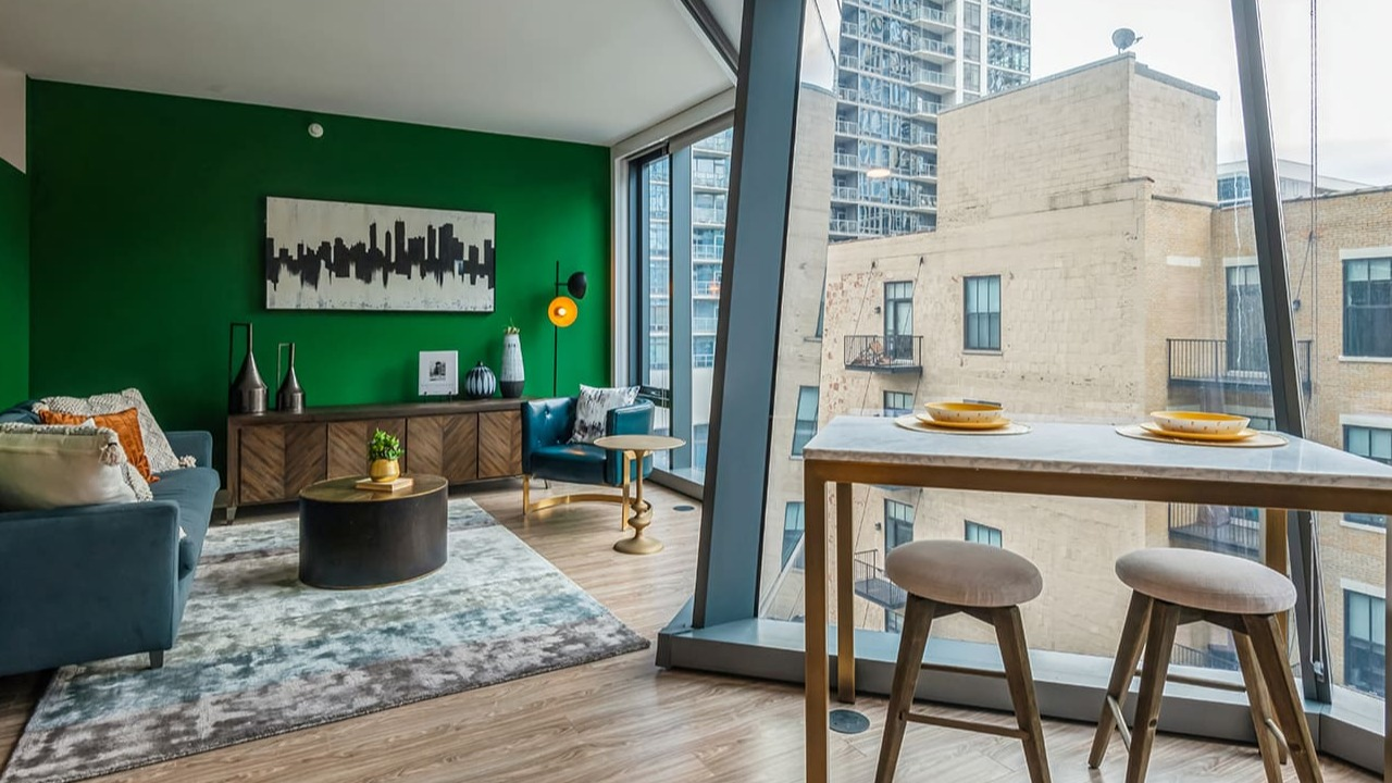 A vibrant living space with green accent wall, modern furniture, and large windows at Arrive Michigan Avenue apartments in Chicago