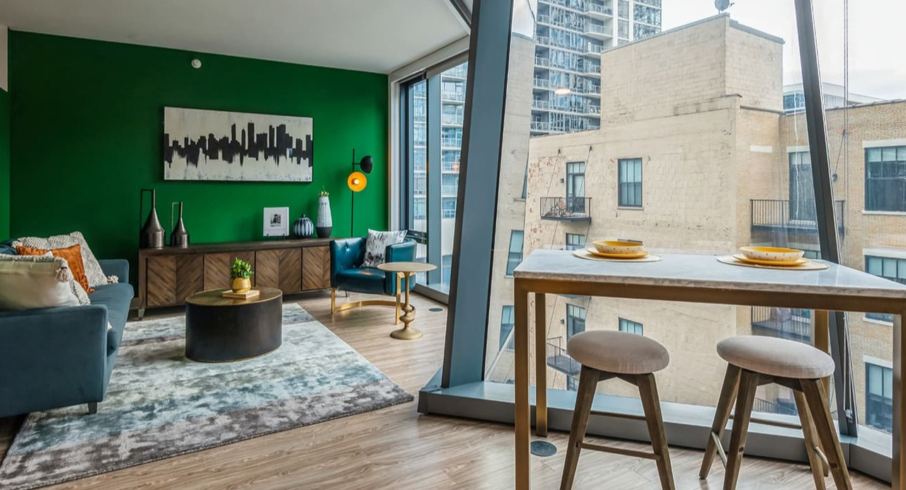 A vibrant living space with green accent wall, modern furniture, and large windows at Arrive Michigan Avenue apartments in Chicago
