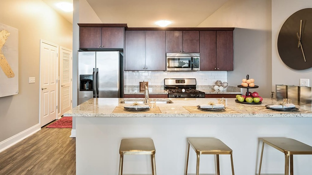 Modern apartment kitchen at Arrive South Loop, featuring stainless steel appliances, granite countertops, and an island with bar seating in Chicago