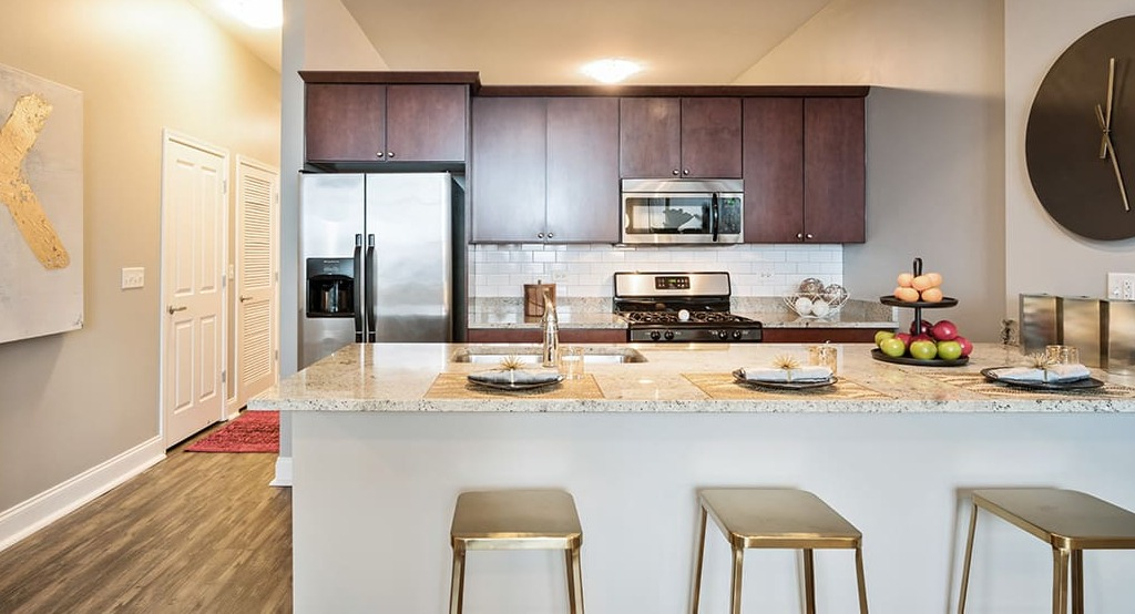 Modern apartment kitchen at Arrive South Loop, featuring stainless steel appliances, granite countertops, and an island with bar seating in Chicago