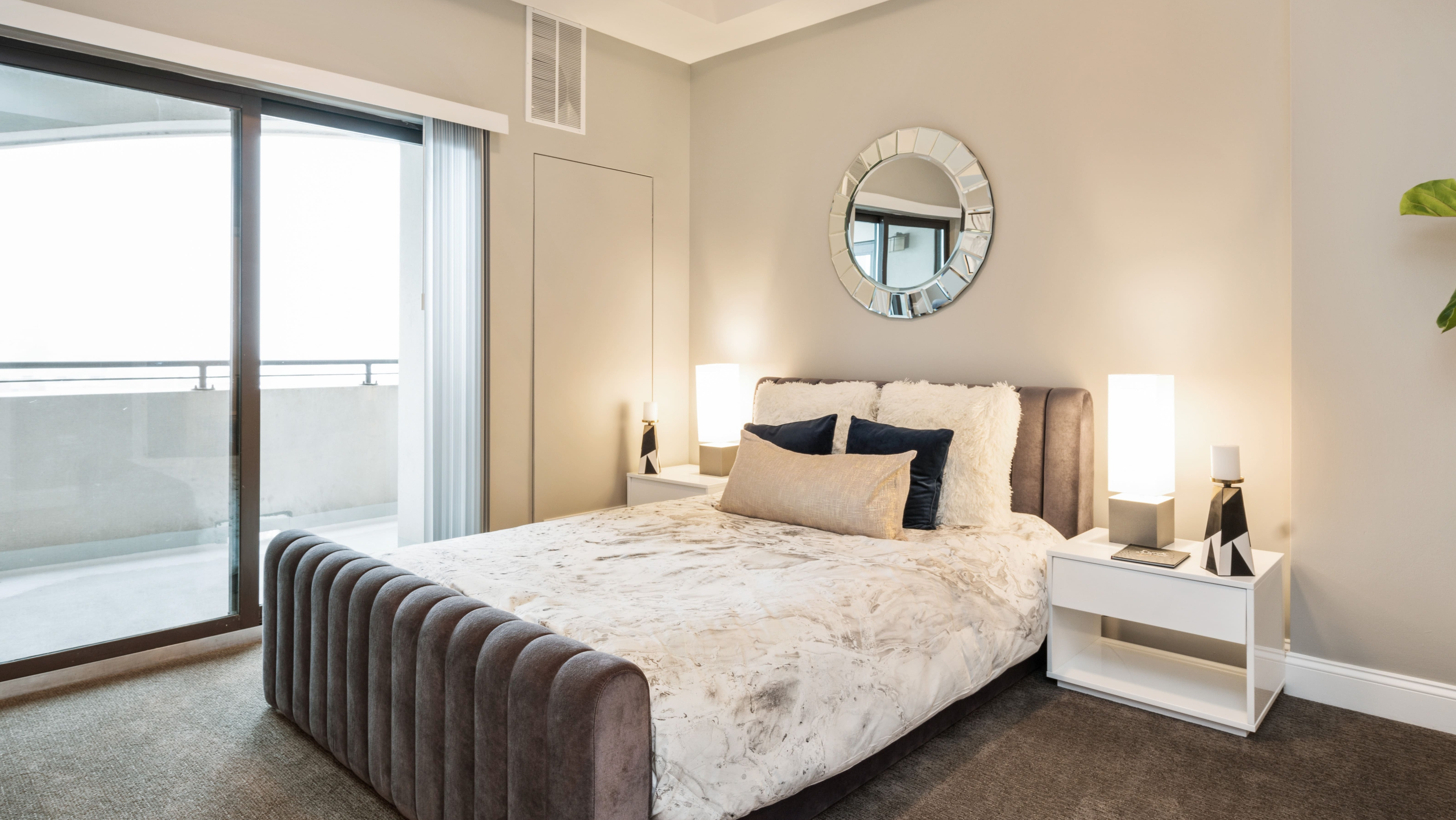 Cozy bedroom with a plush bed, stylish decor, and a private balcony offering city views at Arrive South Loop apartments in Chicago