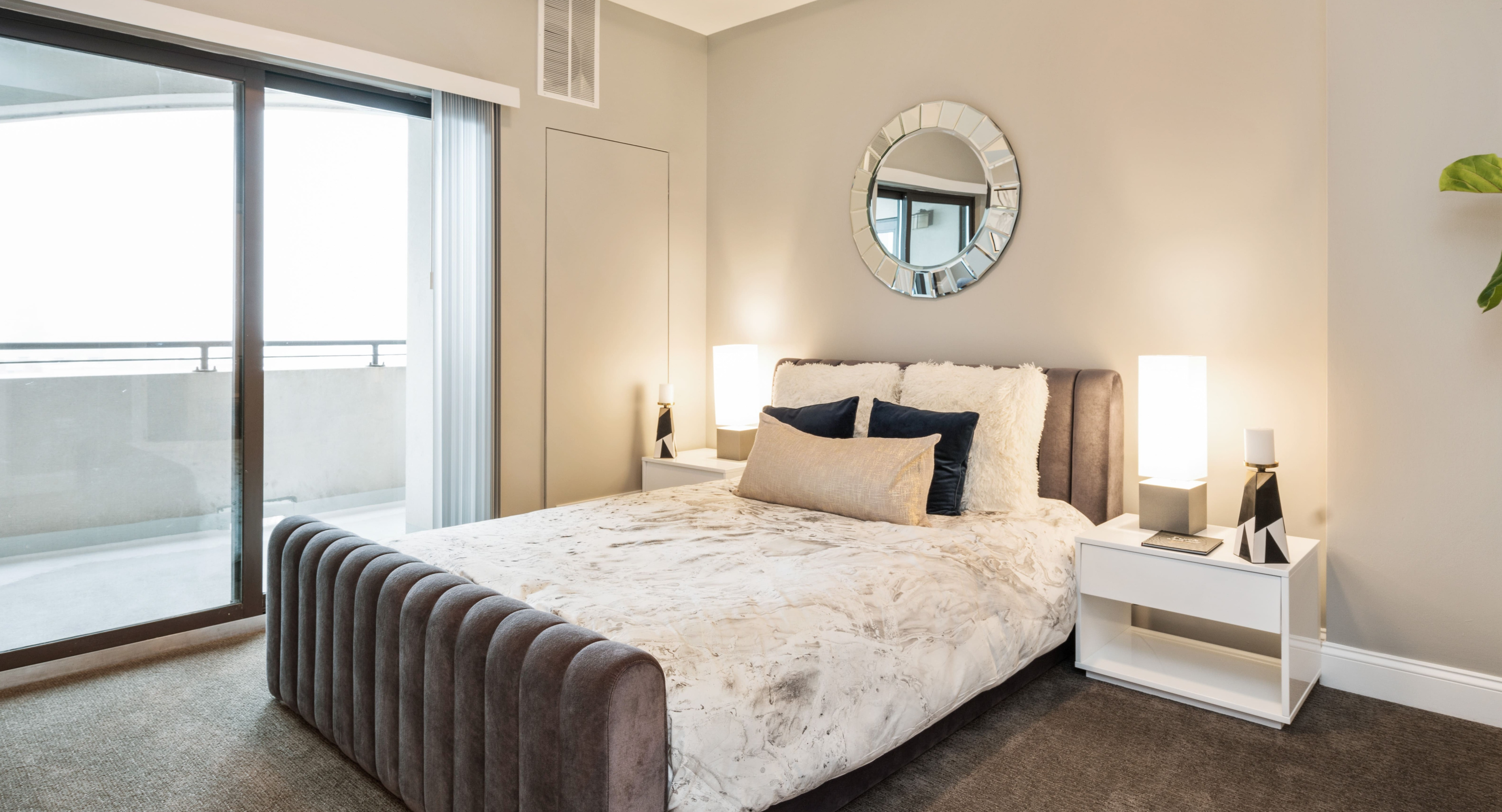 Cozy bedroom with a plush bed, stylish decor, and a private balcony offering city views at Arrive South Loop apartments in Chicago