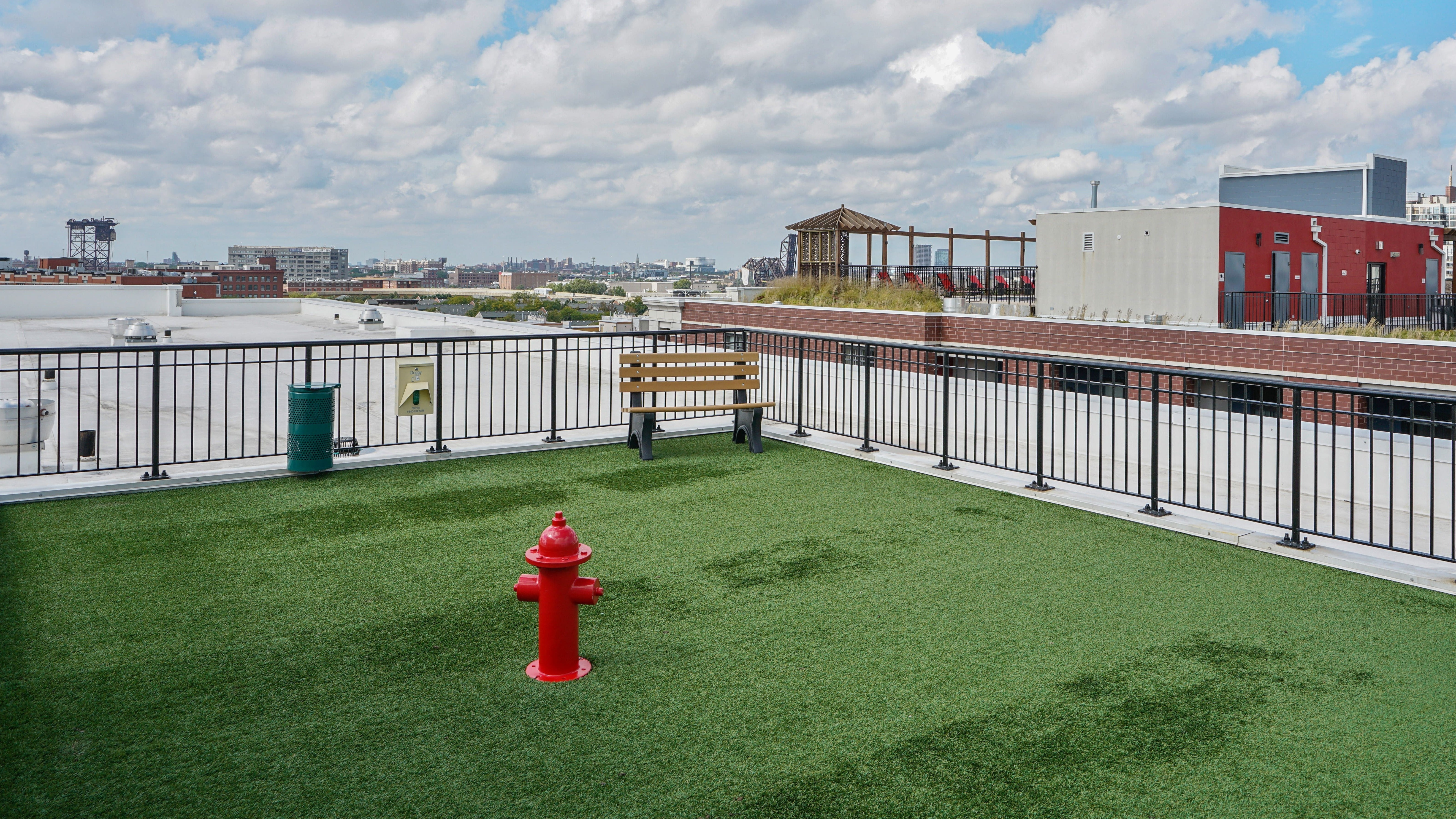 Expansive rooftop dog park at Arrive South Loop apartments with artificial turf, seating, and city skyline views in Chicago