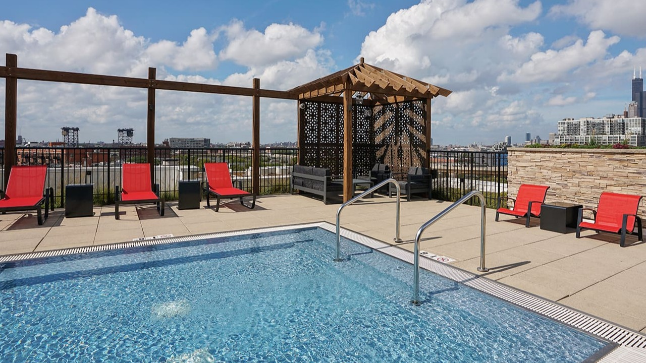 Stunning rooftop pool at Arrive South Loop apartments with lounge chairs, a shaded cabana, and panoramic city skyline views in Chicago