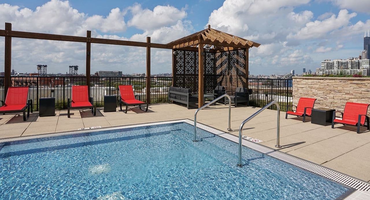 Stunning rooftop pool at Arrive South Loop apartments with lounge chairs, a shaded cabana, and panoramic city skyline views in Chicago
