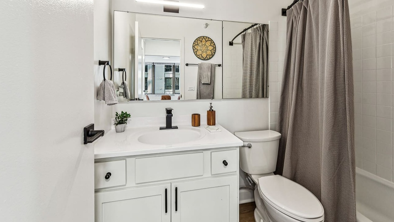 Modern bathroom at Arrive Streeterville with white vanity, dark fixtures, and a glass shower door
