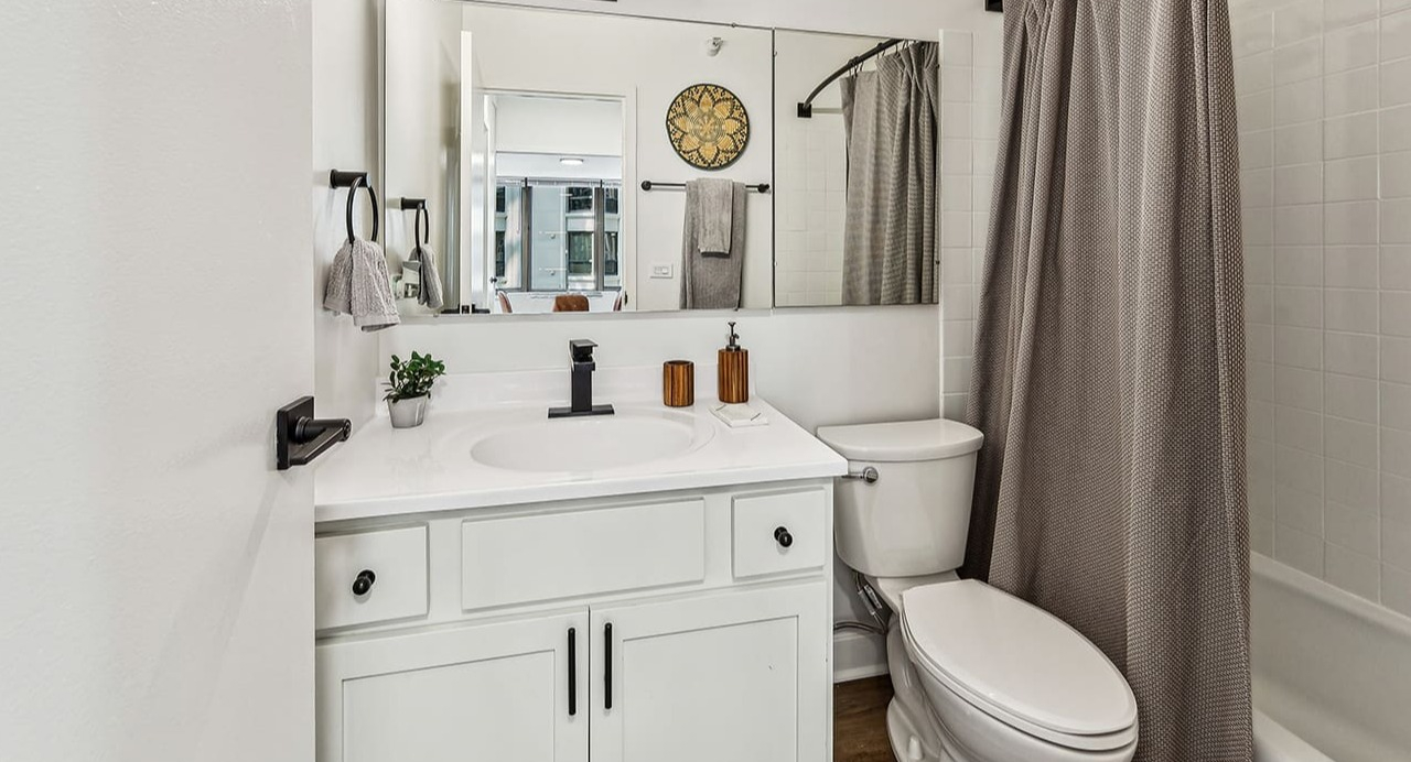 Modern bathroom at Arrive Streeterville with white vanity, dark fixtures, and a glass shower door