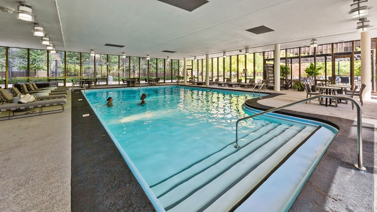 Expansive indoor swimming pool at Arrive Streeterville with surrounding lounge chairs and natural light