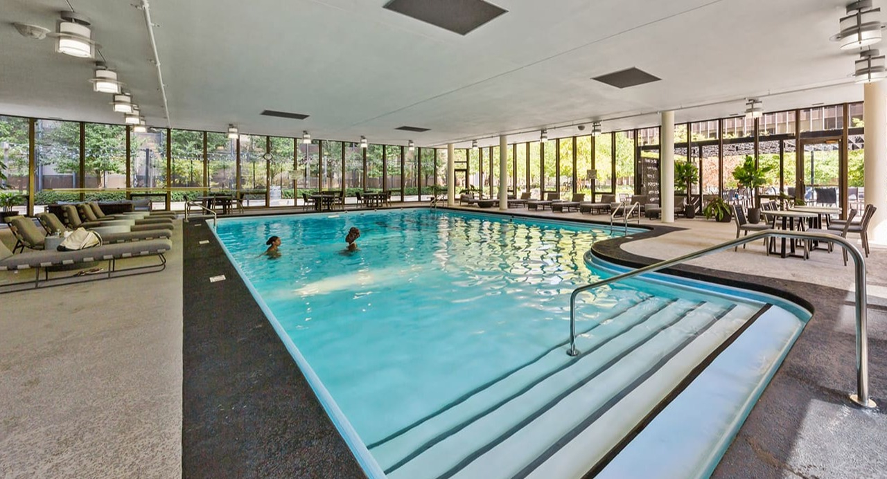 Expansive indoor swimming pool at Arrive Streeterville with surrounding lounge chairs and natural light