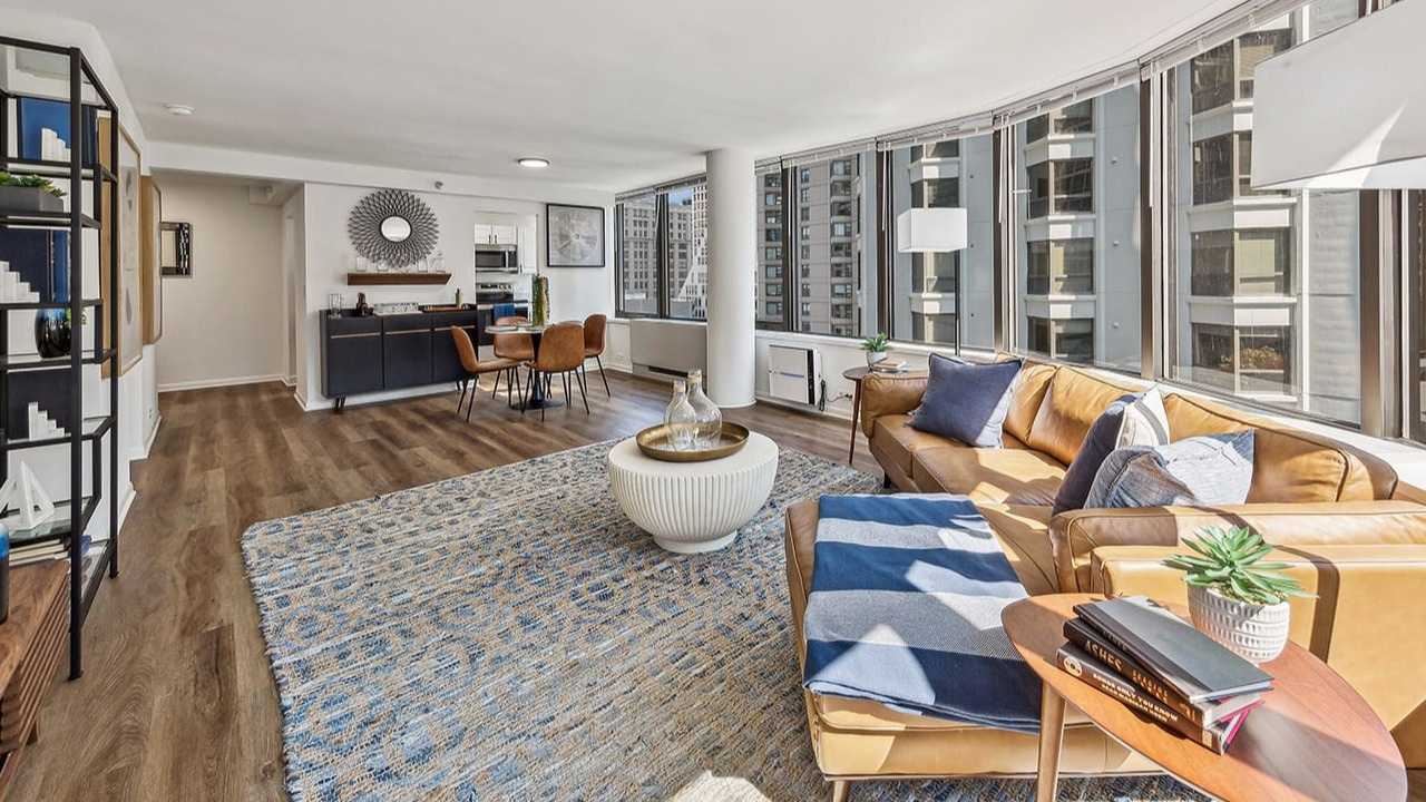 Open-concept living room at Arrive Streeterville with a tan leather sofa, stylish rug, and city views