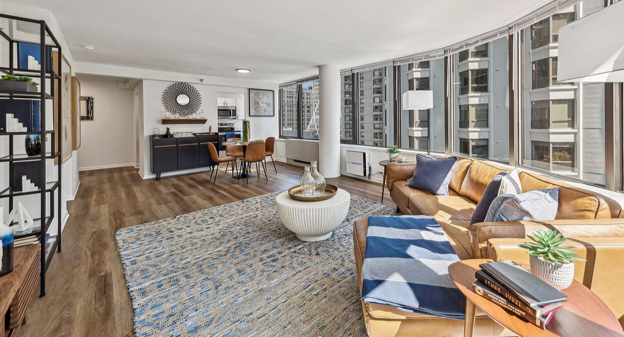 Open-concept living room at Arrive Streeterville with a tan leather sofa, stylish rug, and city views