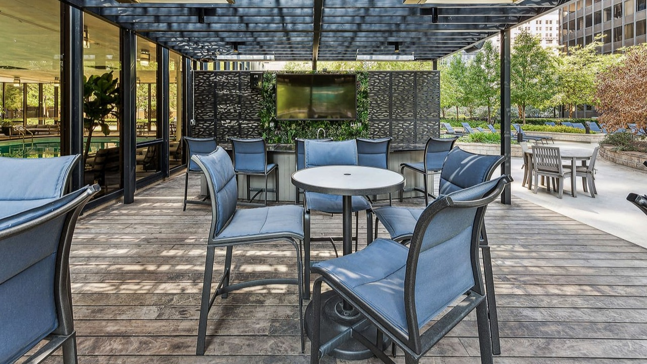 Covered outdoor patio lounge at Arrive Streeterville with comfortable seating and a TV, surrounded by greenery