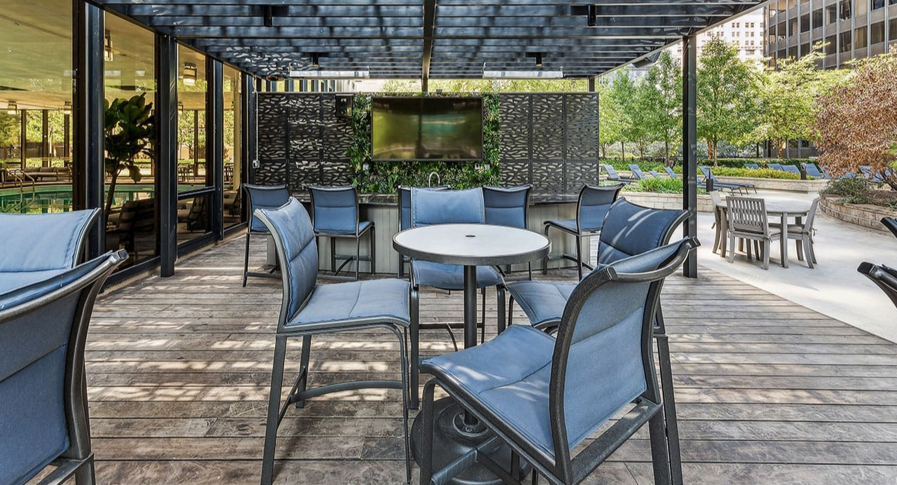 Covered outdoor patio lounge at Arrive Streeterville with comfortable seating and a TV, surrounded by greenery