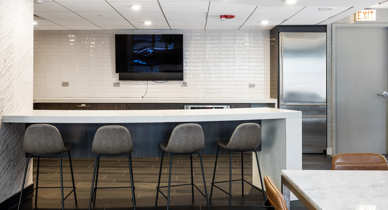 Resident lounge bar area at Arrive Streeterville with bar seating, a television, and modern finishes
