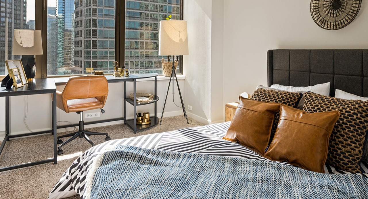 Spacious bedroom at Arrive Streeterville featuring a large bed, a work desk, and ample natural light