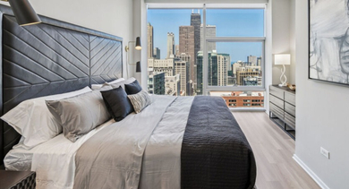 Modern bedroom with a large bed, stylish headboard, and expansive city views from the window at Aston Chicago Apartments