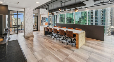 Modern co-working space with a long communal table, office chairs, and large windows overlooking the city at Aston Chicago Apartments