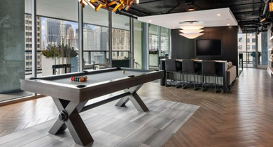 Spacious game room featuring a modern pool table, bar seating, and a comfortable lounge area at Aston Chicago Apartments