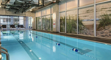 Long indoor lap pool with lane markers and a serene beach-themed mural along the wall at Aston Chicago Apartments