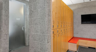 Modern locker room with wooden lockers, a red bench, and a frosted glass steam room door at Aston Chicago Apartments