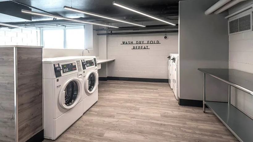 Convenient laundry room with multiple washing machines, folding tables, and bright lighting at Astor House Apartments in Chicago