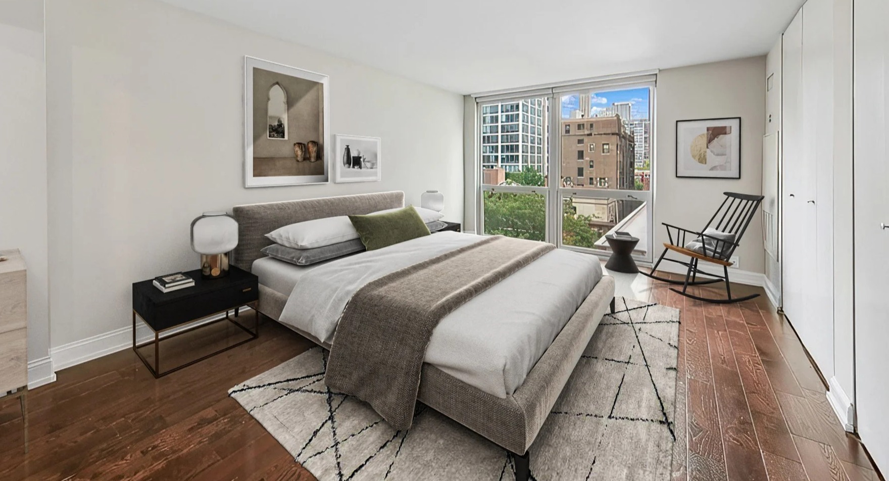 Cozy bedroom with a comfortable bed, minimal decor, and a large window offering city views at Astor House Apartments in Chicago